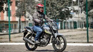 Motociclista equipado com capacete vermelho e casaco cinzento a pilotar uma moto Honda cinzenta numa pista de testes