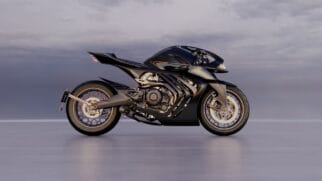 Fotografia de perfil de uma motocicleta superesportiva de luxo da Aston Martin em tom preto e grafite, com design aerodinâmico futurista, motor exposto e jantes de liga leve, posicionada numa pista com céu nublado ao fundo