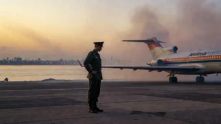 Avião em pista de aeroporto urbano ao entardecer com fumaça ao fundo, evocando o atentado de 1975 no Aeroparque de Buenos Aires