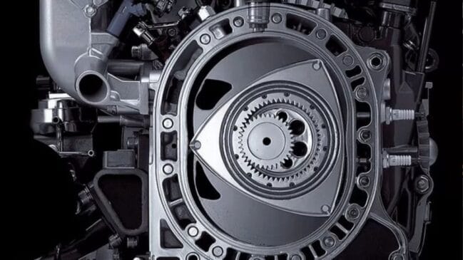 Fotografia em plano aproximado e detalhado da secção interna de um motor rotativo Wankel sem pistões, exibindo o rotor triangular com engrenagens centrais no interior da carcaça metálica
