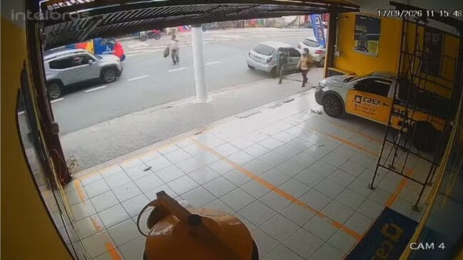 Fotografia de câmara de segurança (CFTV) em ângulo superior a partir do interior de um estabelecimento comercial virado para a rua. Na calçada e via pública, observam-se peões a caminhar, veículos estacionados e em circulação sob luz do dia. No canto superior direito, visualiza-se o carimbo de data e hora do Registo (17/09/2026)