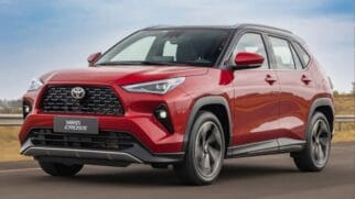 Fotografia de um automóvel SUV Toyota Yaris Cross vermelho com tejadilho preto em circulação numa estrada, visto em perspetiva de três quartos dianteira