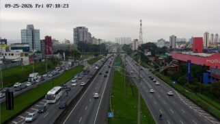Imagem de câmara de monitorização do tráfego na Rodovia Anchieta em São Paulo, mostrando pistas com trânsito intenso num dos sentidos e edifícios urbanos ao fundo sob céu nublado