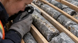Geólogo com capacete examinando testemunhos de perfuração em caixas, diante de uma mina montanhosa nos Andes argentinos.