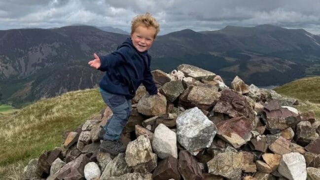Navy Moores posa sobre um marco de pedras durante a jornada que o levou aos 214 picos do Lake District aos três anos (Foto: Arquivo pessoal/Família Moores)
