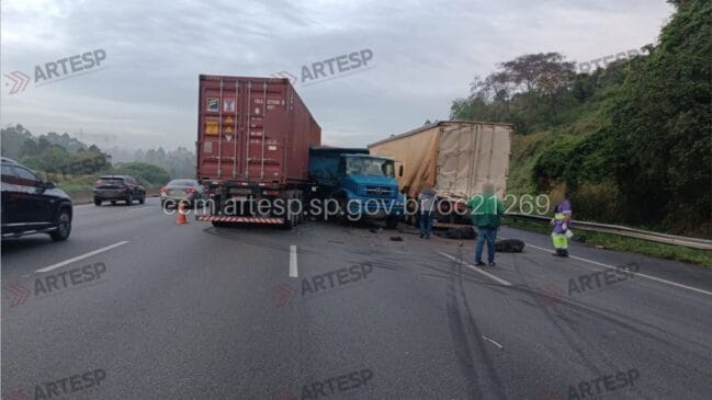 Fotografia de um acidente rodoviário na Rodovia dos Bandeirantes envolvendo dois camiões de carga imobilizados e a bloquear vias da autoestrada, com cones de sinalização, marcas de travagem e trânsito condicionado ao fundo