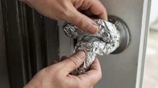 Mãos enrolando papel alumínio no puxador externo de uma porta residencial