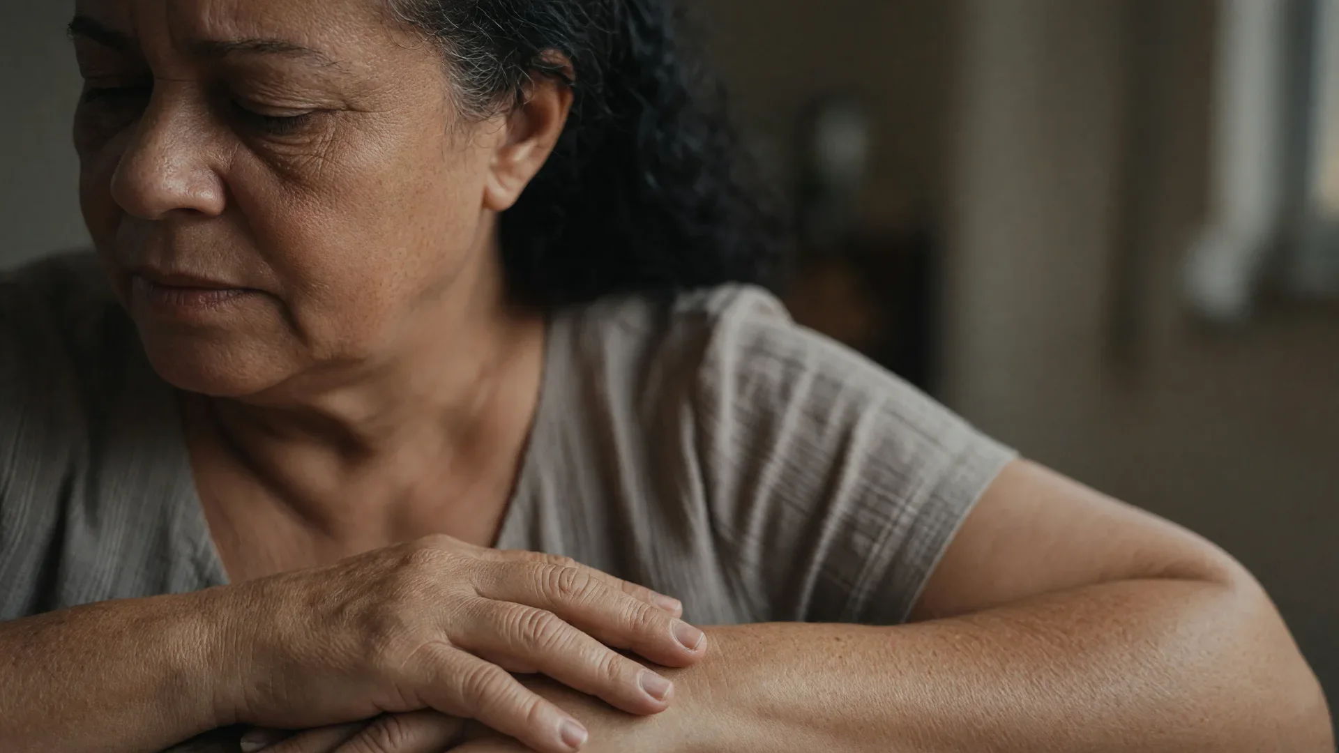 Enquadramento fechado do rosto e das mãos de uma mulher madura durante atendimento, luz lateral suave, clima documental de cuidado e envelhecimento feminino, sem elementos gráficos