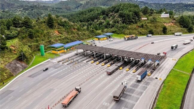 Vista aérea de uma praça de pedágio na Rodovia Régis Bittencourt, operada pela Arteris, com veículos e camiões nas cabinas de cobrança e uma paisagem arborizada ao redor