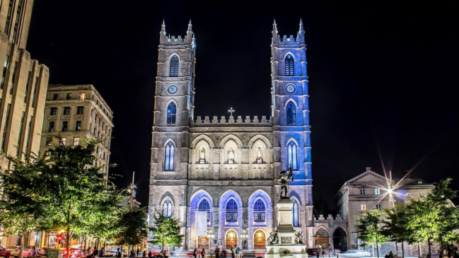 Iluminação noturna destaca as torres neogóticas e os detalhes arquitetônicos da Basílica de Notre-Dame, um dos monumentos mais conhecidos de Montreal (Foto: Michael Vesia – Wikimedia Commons)