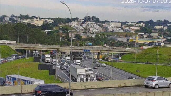 Fotografia de trânsito intenso e congestionamento matinal numa via expressa em São Paulo, com filas densas de automóveis e camiões sob um viaduto rodoviário, registada a 7 de outubro de 2026
