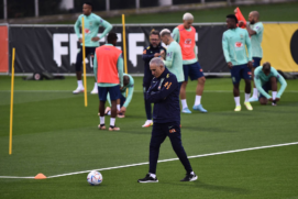 Tite com a bola, durante treinamento do Brasil na Itália, enquanto, ao fundo, jogadores fazem trabalho físico; seleção embarca para o Qatar no sábado (19)