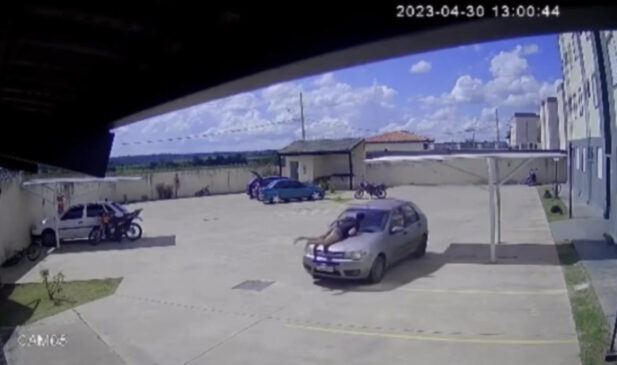 Imagens da câmera de segurança mostra o momento em que o homem arrasta a vítima no capô do carro
