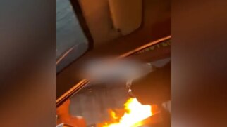 O homem que ocupa o banco do carona aciona uma embalagem aerossol sobre o fogo, criando uma grande chama, que vai em cheio em Beatriz