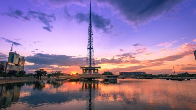 Torre de TV e espelho d'água ao entardecer, refletindo as cores características do céu de Brasília.