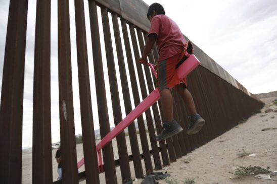 Crianças e adultos brincam na gangorra instalada entre a cerca da fronteira que divide o México dos Estados Unidos