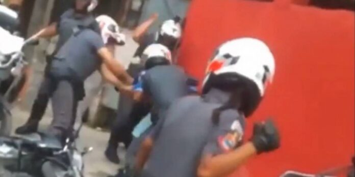 Vídeo mostra uma pessoa cercada por ao menos 5 policiais, todos com capacetes; 3 deles desferem socos e joelhadas no homem